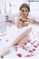 A woman sitting in a bathtub with rose petals on the floor.