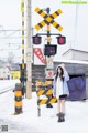 A woman standing next to a railroad crossing in the snow.