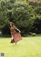 A woman in a brown dress is walking in the grass.