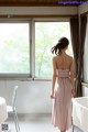 A woman in a pink dress standing in front of a window.