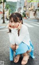 A young woman crouching down on the street with her hand on her chin.