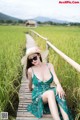 A woman in a green dress and hat sitting on a wooden bridge.