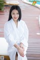 A woman in a white robe sitting by a pool.